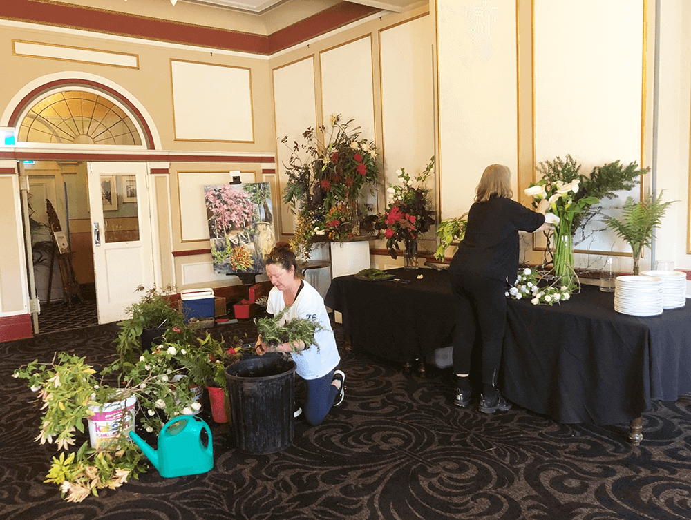 Jessica Lawn and Pennie Steel arranging flowers in Carrington Ballroom for launch of Artists for Treeline Lurline. Pennie's painting of Lurline Street Spring Garden in background. Photo Kerry Brown.